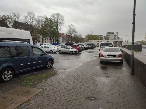 Parkende Autos auf einem Parkplatz in der Nähe vom Rhein. Rechts ist der Parkplatz durch eine Mauer abgetrennt.