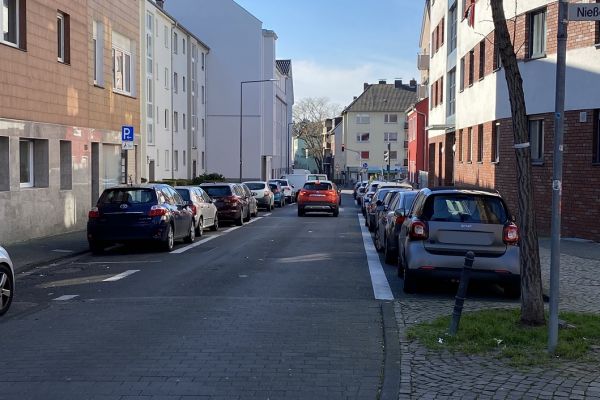 Zu sehen ist der Bereich Höfestraße zwischen Nießen- und Kalk-Mülheimer Straße. Links und rechts parken Autos auf einem Parkstreifen. Auf beiden Seiten ist ein Bürgersteig.