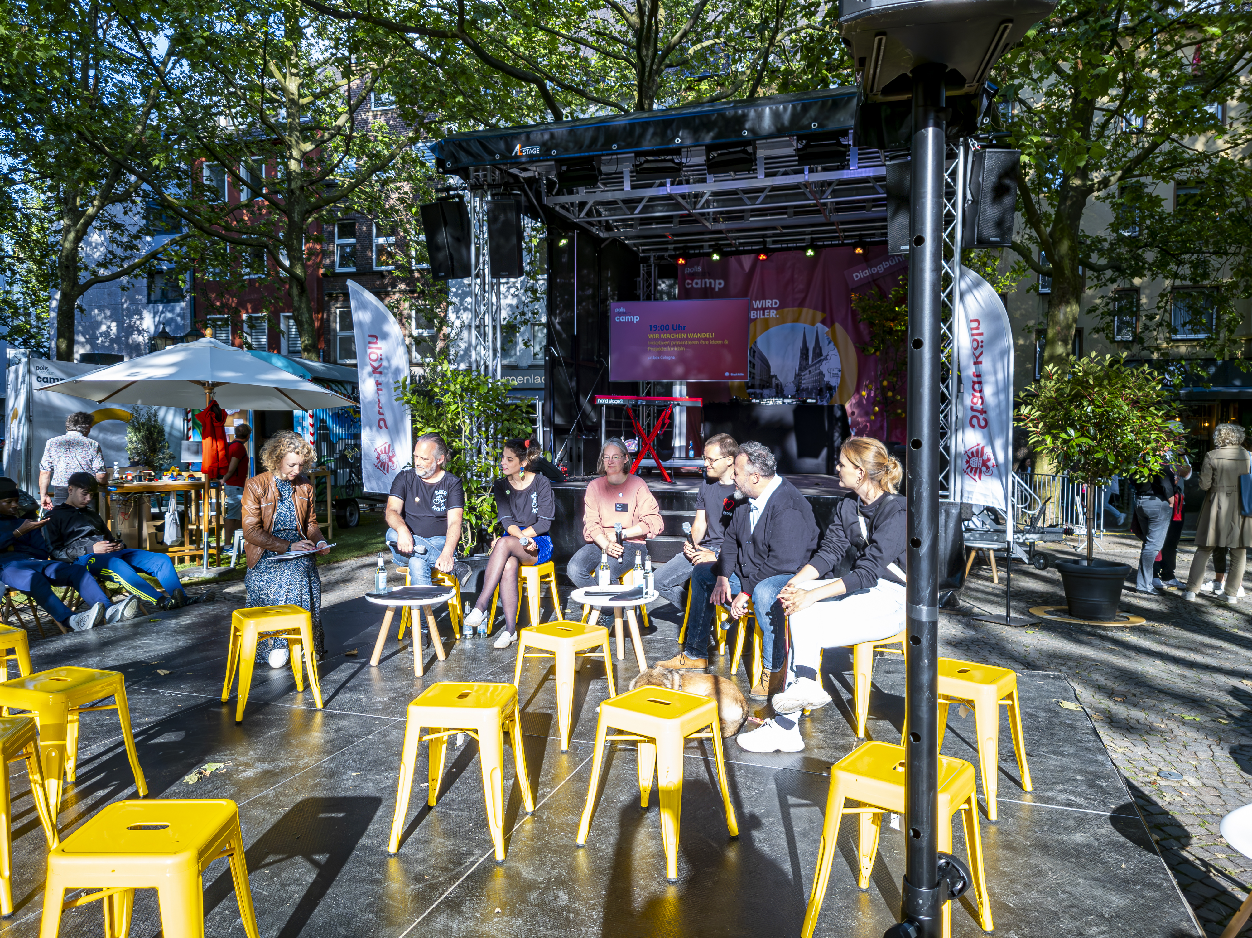 Menschen sitzen auf Stühlen im Kreis auf dem Rudolfplatz und diskutieren