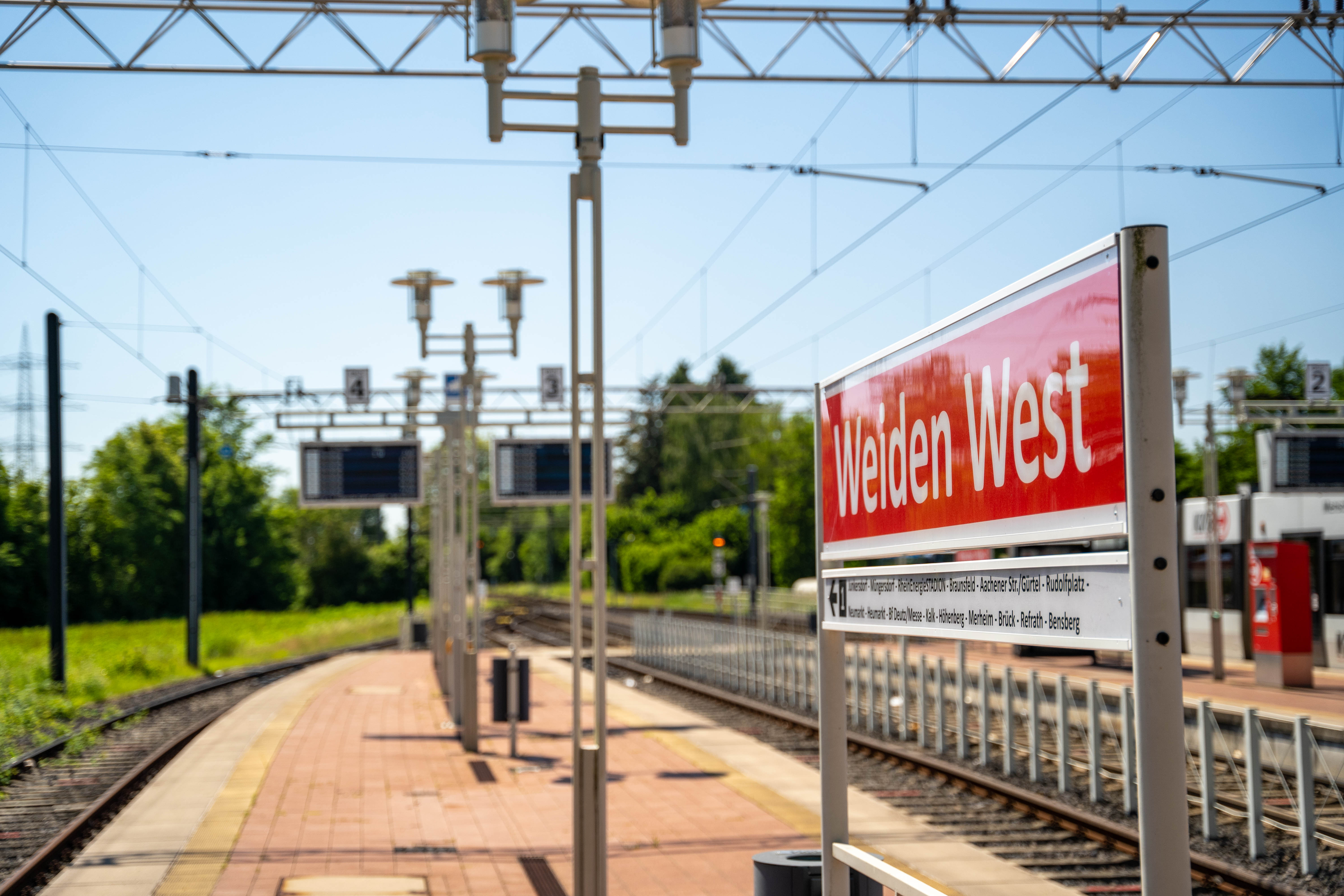 Alternativtext Bild:	Seitlicher Blick auf das Haltestellenschild Weiden West mit Schienen und Grünfläche im Hintergrund