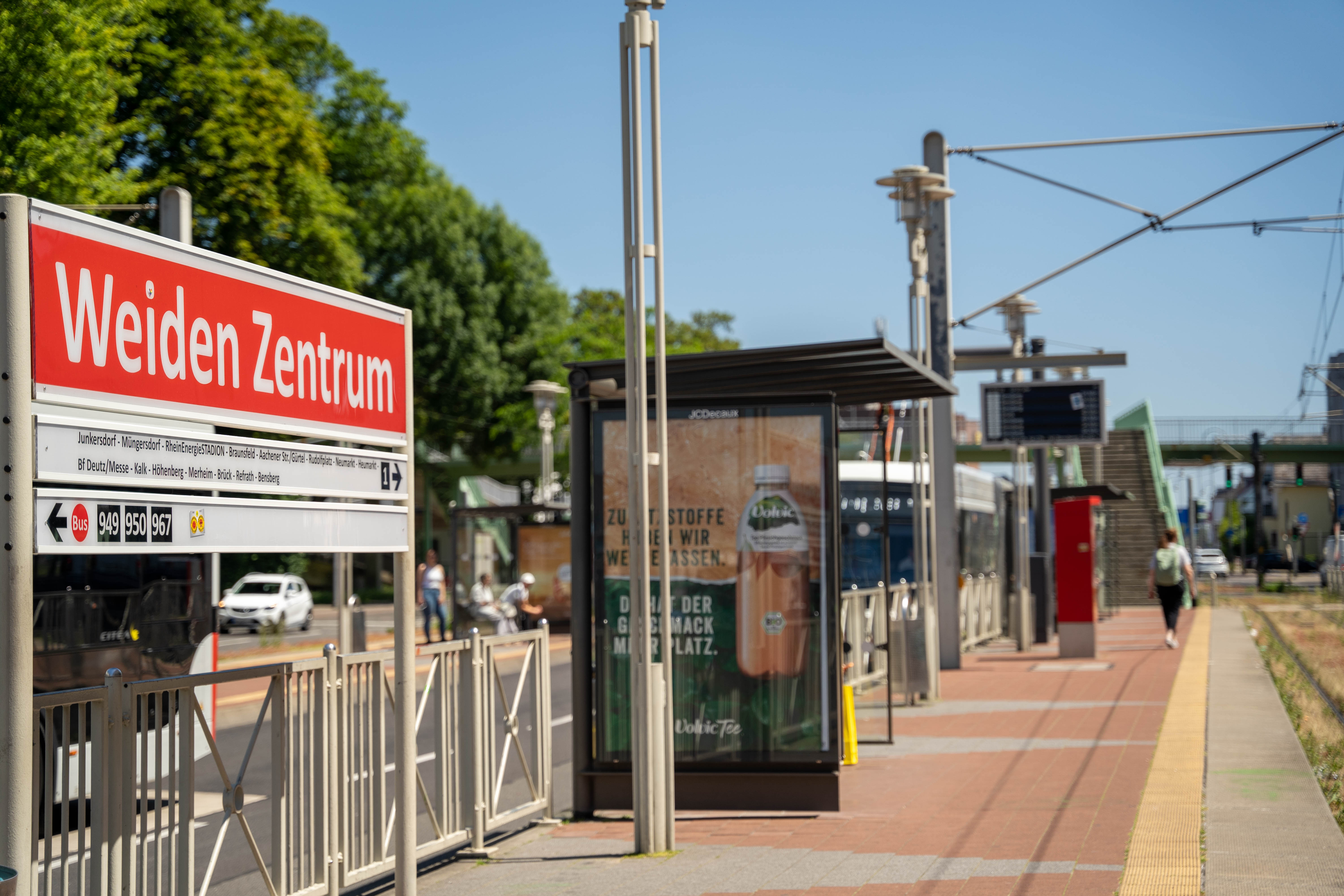 Seitlicher Blick vom Bahnsteig auf das Haltestellenschild Weiden Zentrum mit Blick auf die Fußgängerbrücke 