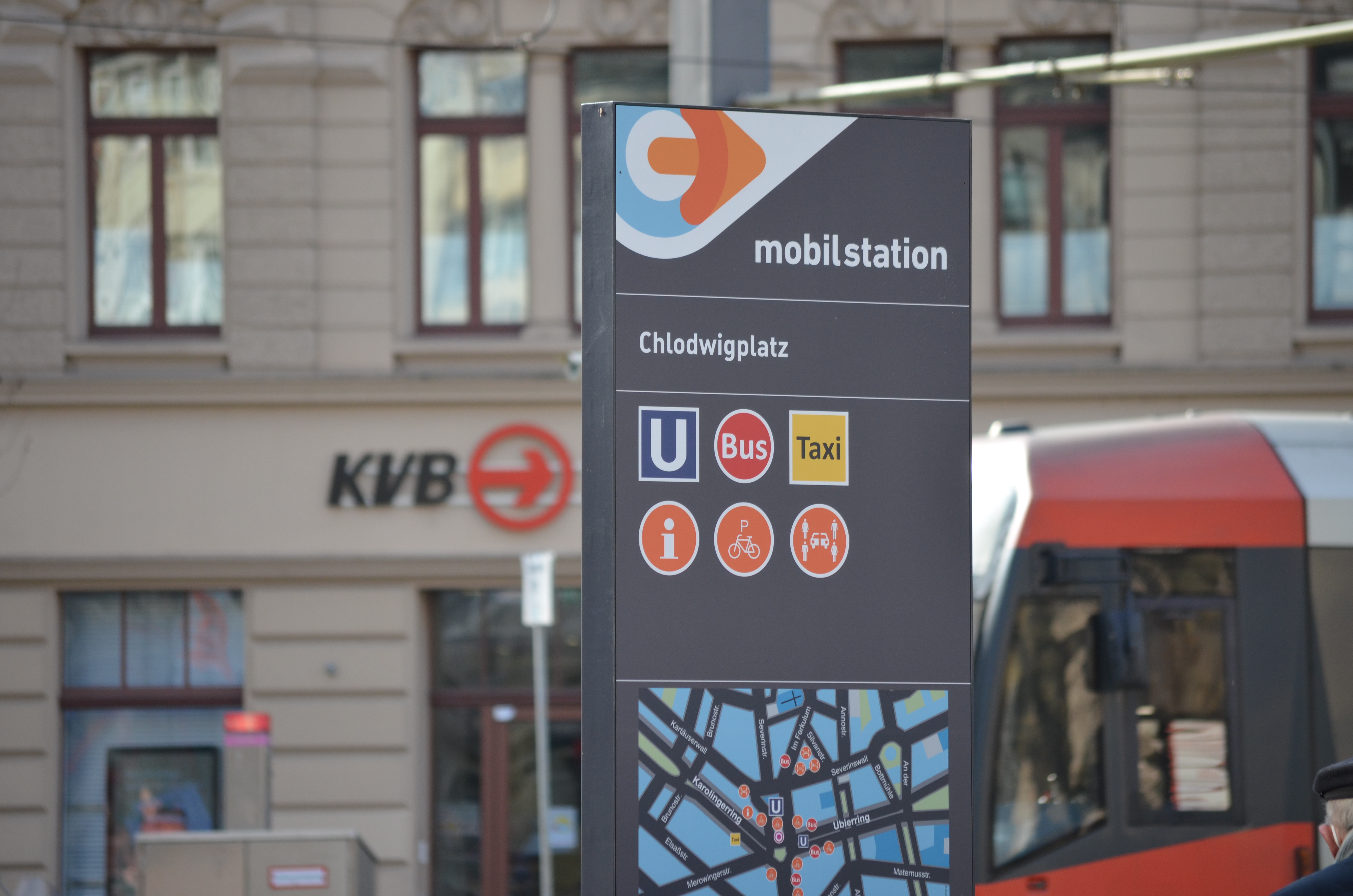 Schild einer Mobilstation am Chlodwigplatz in Köln. Auf dem Schild sind die Zeichen für U-Bahn, Bus und Taxi sowie ein Stadtplan.