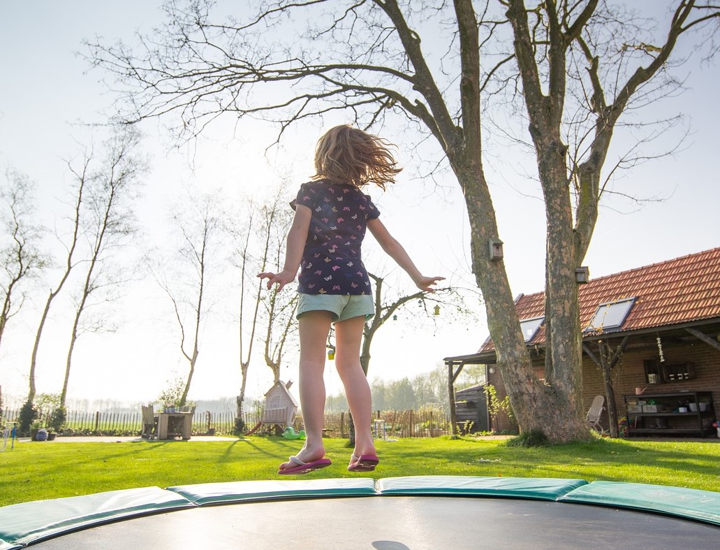 Ein Kind hüpft auf einem Trampolin in einem Garten.