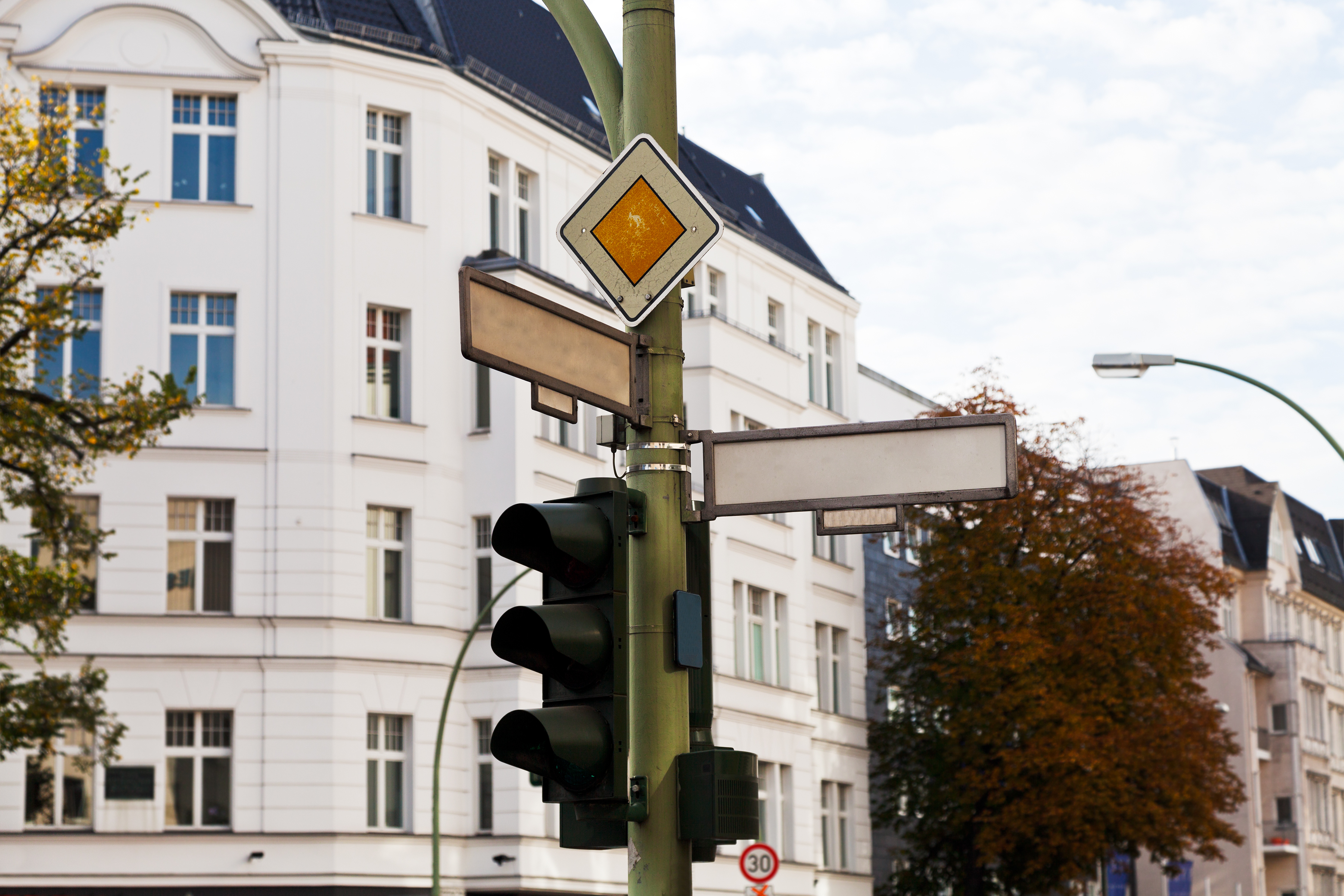 Das Bild zeigt eine Straßenkreuzung inklusive einer Ampel und zwei unbeschrifteten Straßenschildern. 