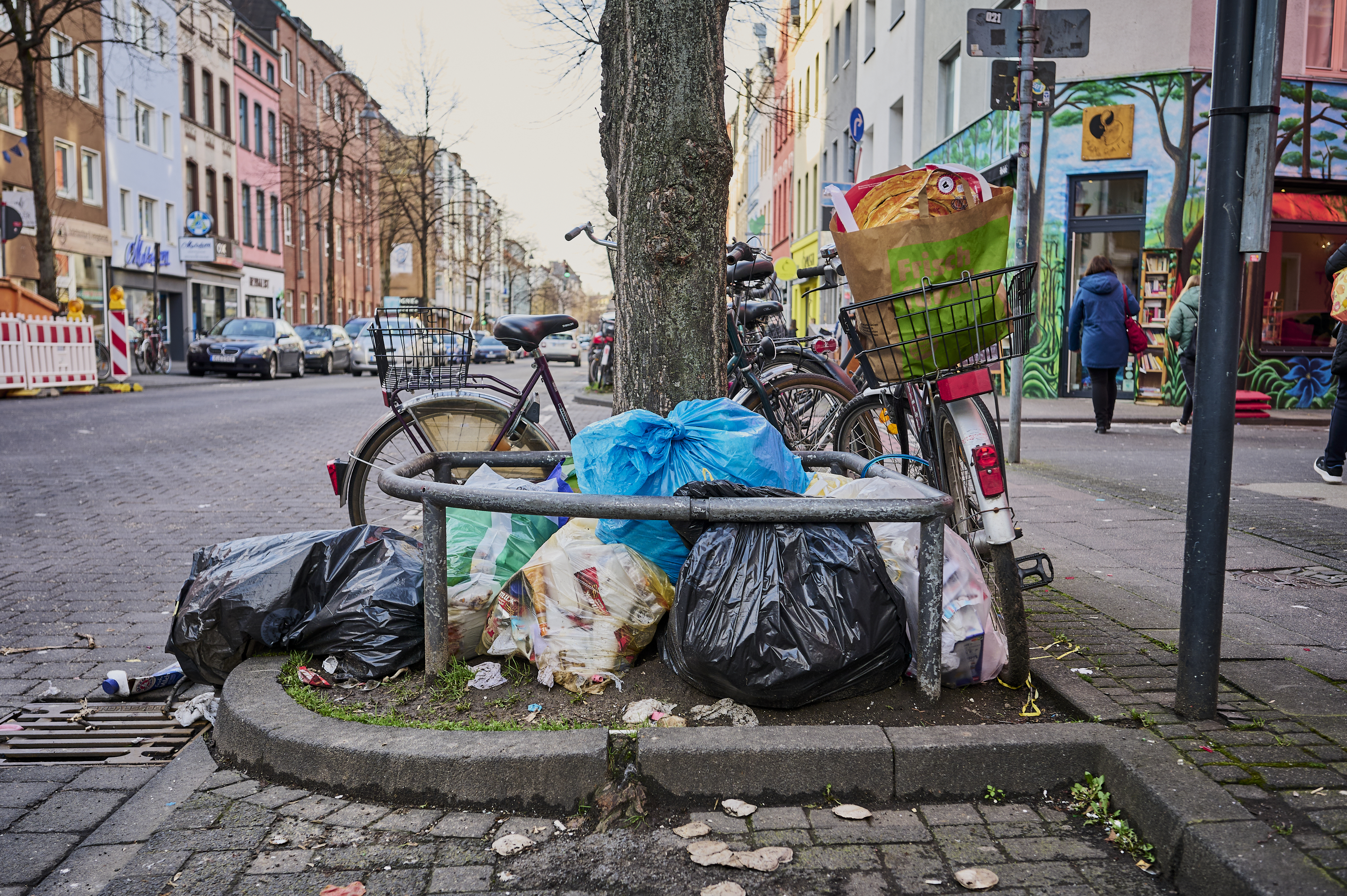 Müllsäcke und loser Müll liegen auf der Straße und einer Baumscheibe.