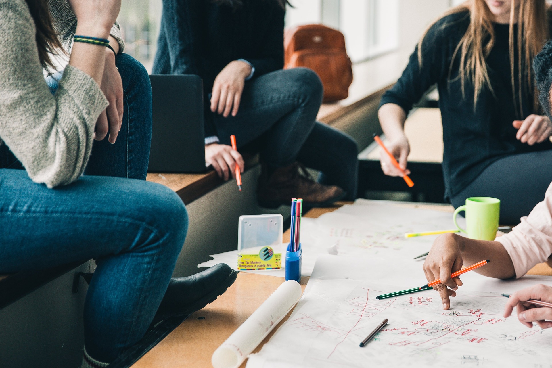 Schülerinnen und Schüler arbeiten gemeinsam an einem Gruppentisch mit bunten Stiften und Papier. 